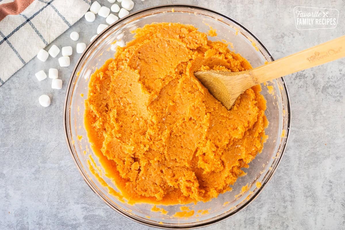 Glass mixing bowl with sweet potato mixture and a wooden spoon.