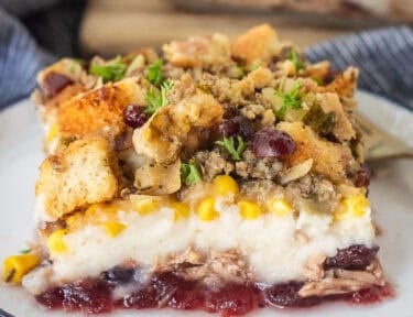Plate with a slice of Thanksgiving Leftover Casserole with layers of turkey, cranberry sauce, mashed potatoes, turkey gravy, corn and sausage stuffing.