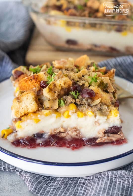 Plate with a slice of Thanksgiving Leftover Casserole with layers of turkey, cranberry sauce, mashed potatoes, turkey gravy, corn and sausage stuffing.