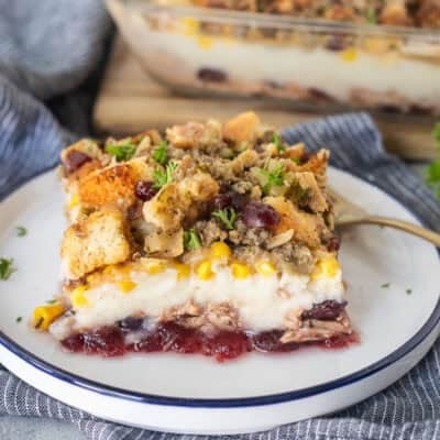 Plate with a slice of Thanksgiving Leftover Casserole with layers of turkey, cranberry sauce, mashed potatoes, turkey gravy, corn and sausage stuffing.