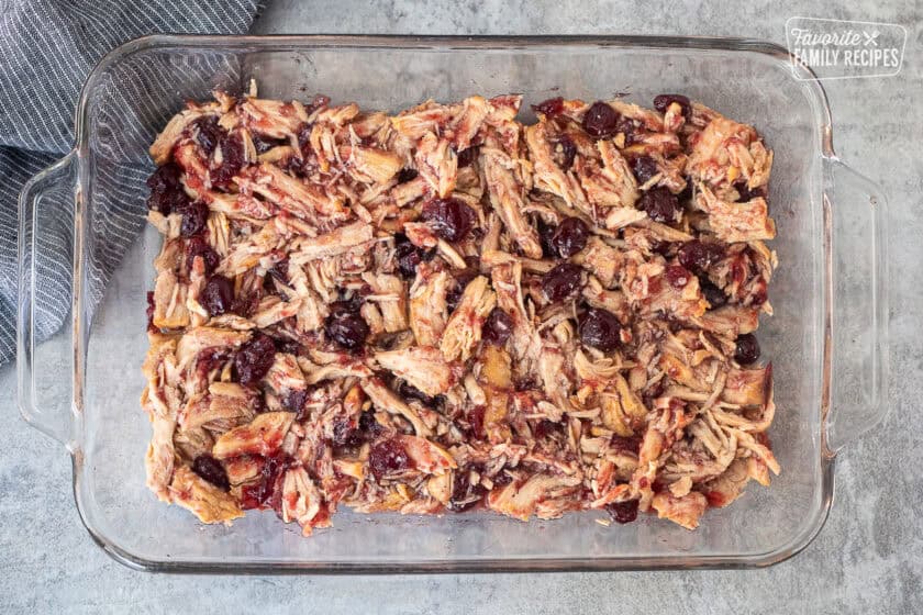 Glass baking dish with shredded turkey mixed with cranberry sauce.