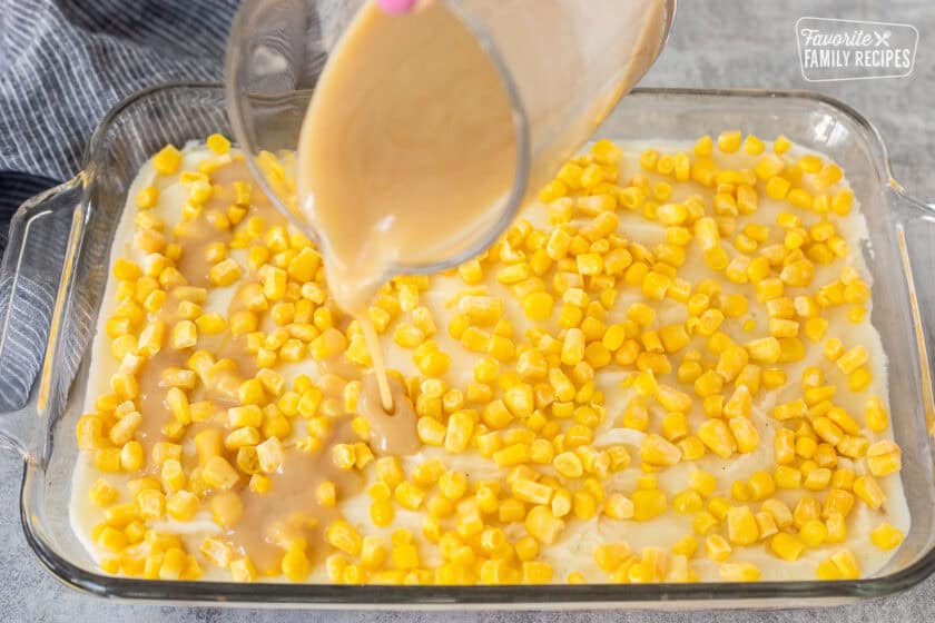 Pouring turkey gravy on top of mashed potato and corn layer.