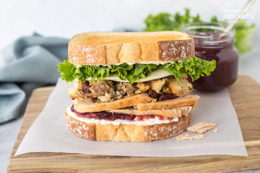 Thanksgiving leftover sandwich on two slices of toasted white bread with cream cheese, cranberry sauce, sliced turkey, sausage stuffing, provolone cheese, lettuce and mayo.