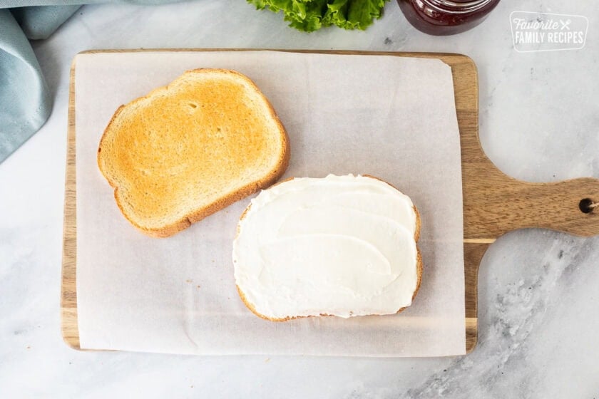 Two slices of toasted white bread with spread cream cheese on one slice.