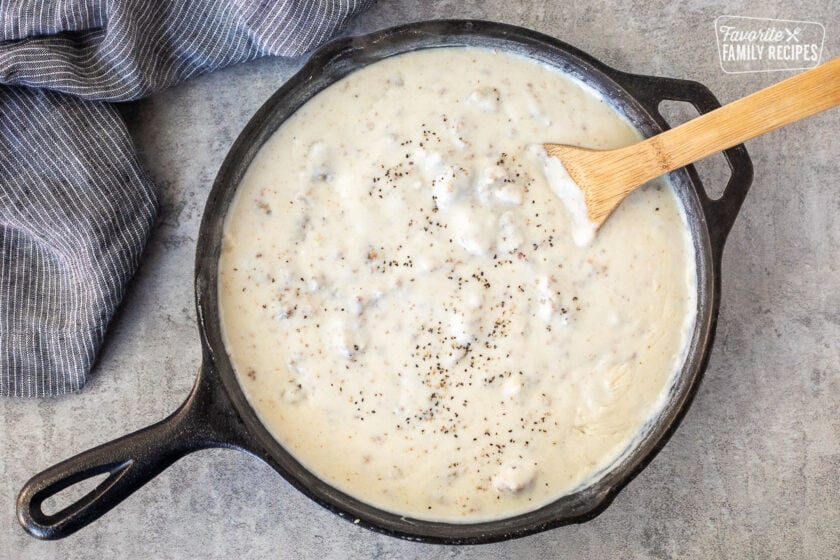 Skillet with sausage gravy and mixing in cracked black pepper with wooden spoon.