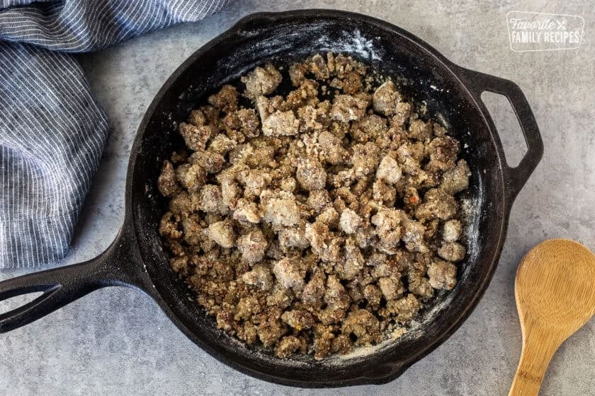 Skillet with cooked sausage combined with flour to make the gravy for biscuits and gravy. Wooden spoon on the side.