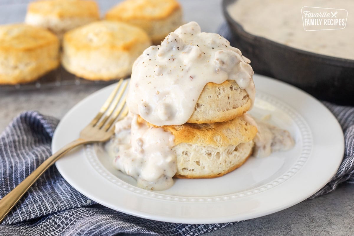 A plate with two biscuits stacked on top of each other with sausage gravy over the top.