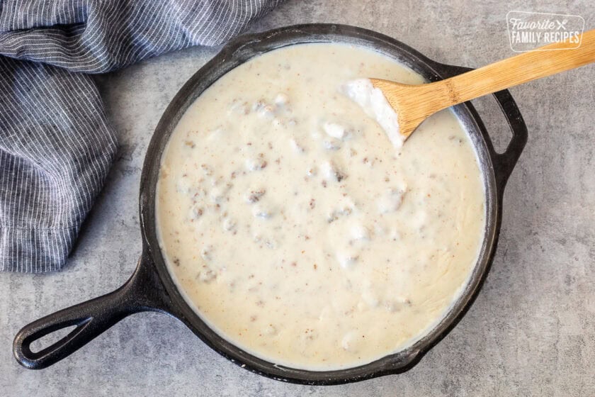 Skillet with thickened sausage gravy and a wooden spoon.