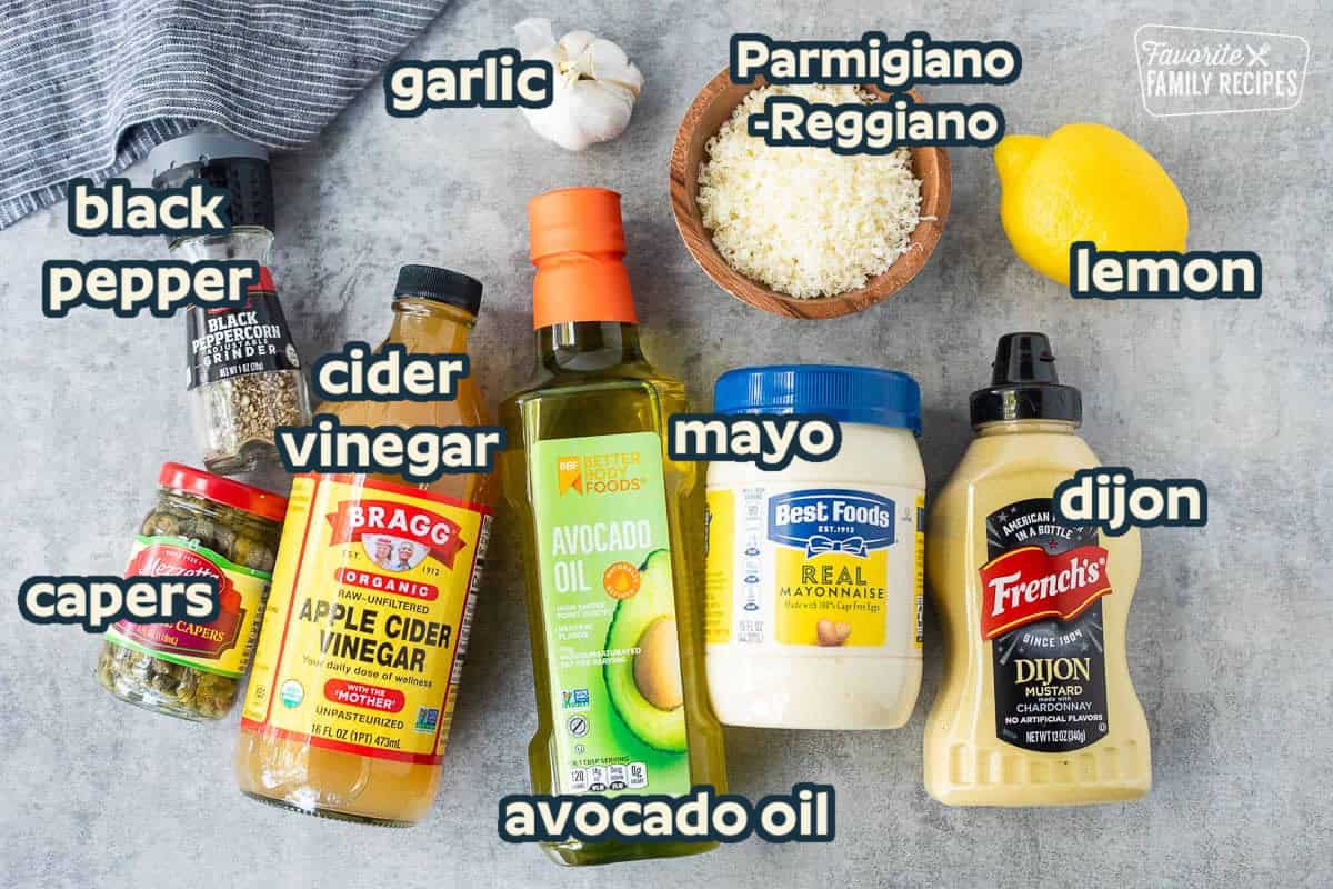 Ingredients to make Caesar Salad Dressing including mayonnaise, avocado oil, Dijon mustard, apple cider vinegar, capers, black pepper, grated cheese, garlic and lemon.
