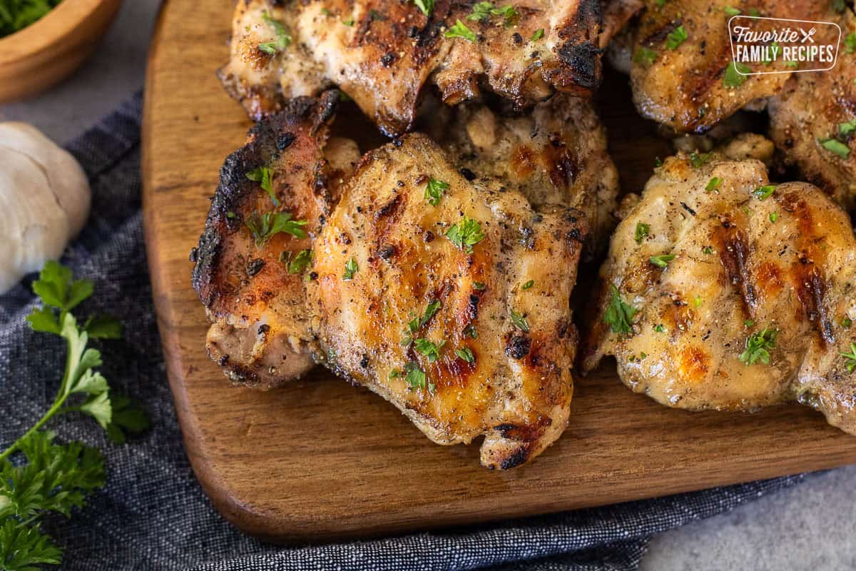 Barbecue marinaded chicken thighs on a cutting board and garnished with parsley.
