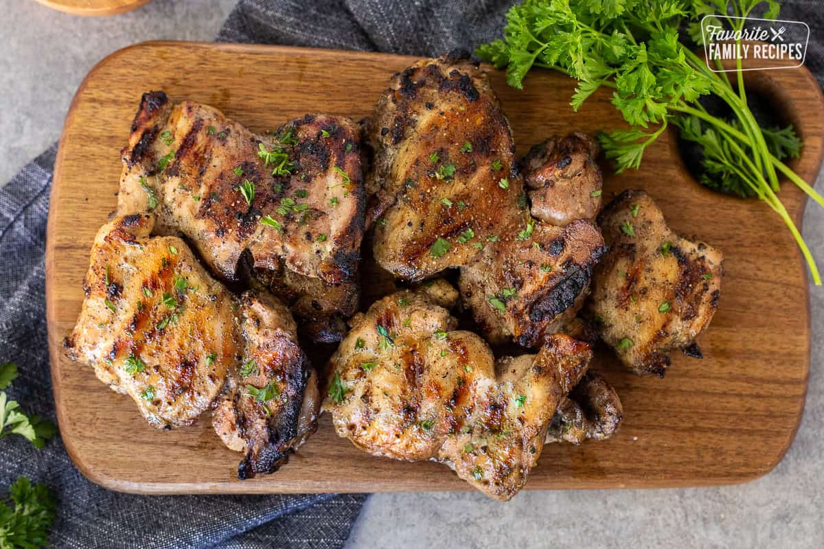 Barbecue marinaded chicken thighs on a cutting board and garnished with parsley.