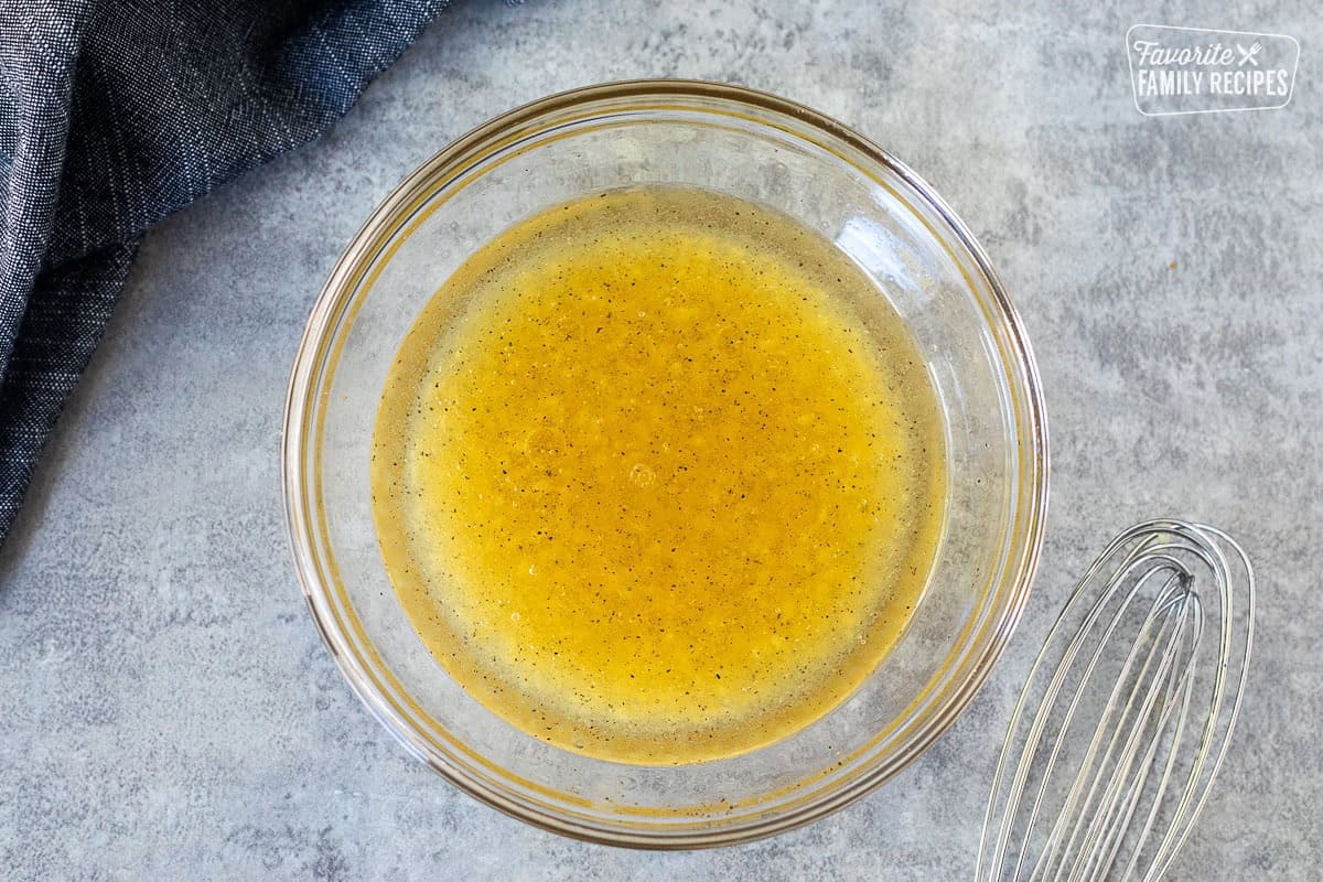 Glass mixing bowl with chicken thigh marinade and whisk on the side.