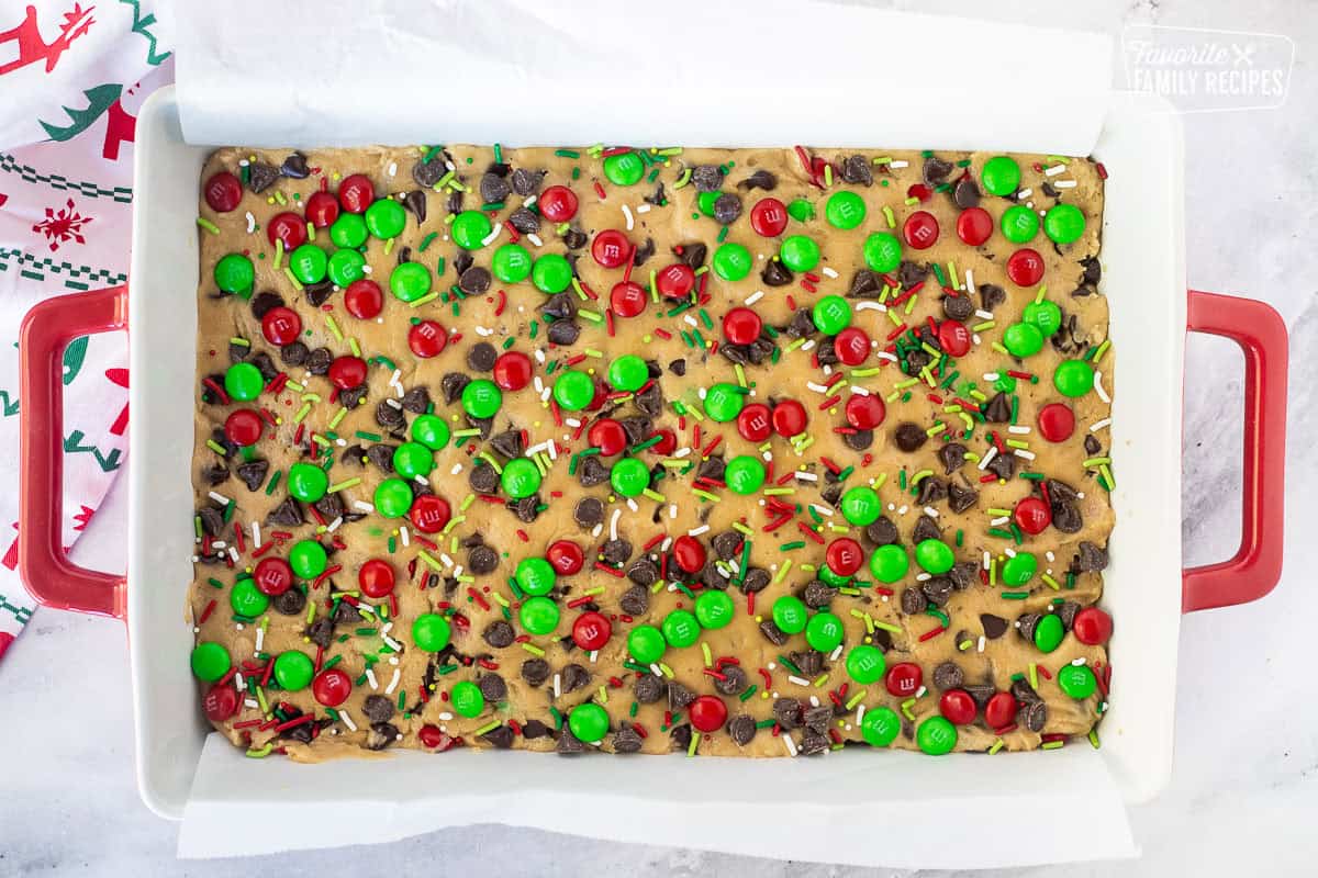 Chocolate chips, sprinkles and chocolate candies added to top of Christmas cookie bar dough.