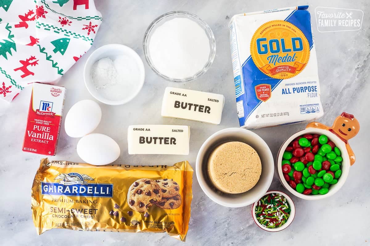 Ingredients to make Christmas Cookie Bars including flour, butter, chocolate candies, brown sugar, sprinkles, butter, sugar, eggs, butter, chocolate chips, baking soda, baking powder, salt and vanilla extract.