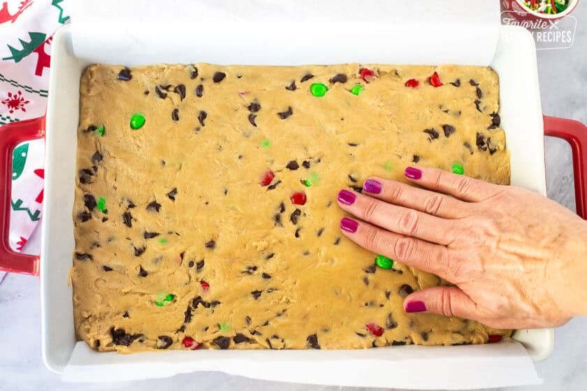 Hand pressing Christmas cookie dough into dish lined with parchment paper.