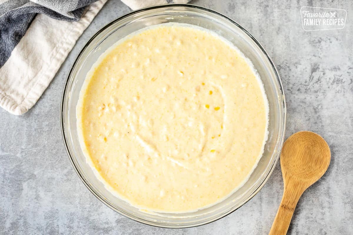 Glass mixing bowl with cornbread pudding batter. Wooden spoon on the side.
