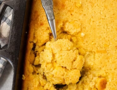Spoon resting in baking dish with cornbread pudding.