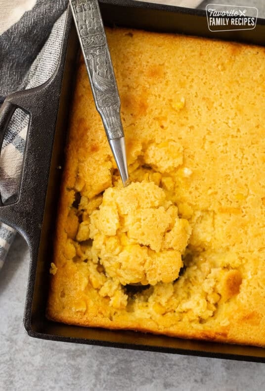 Spoon resting in baking dish with cornbread pudding.