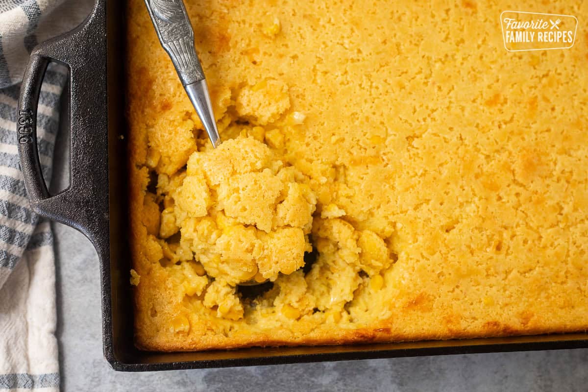 Spoon resting in baking dish with cornbread pudding.