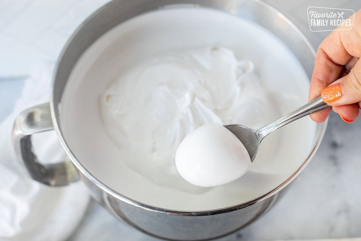 Scoop of divinity mixture in a spoon over mixing bowl.