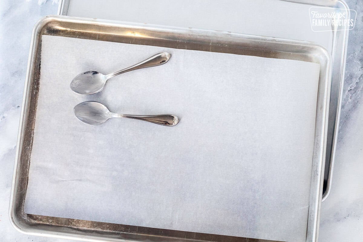 Prepared cookie sheets with parchment paper and spoons covered in butter.