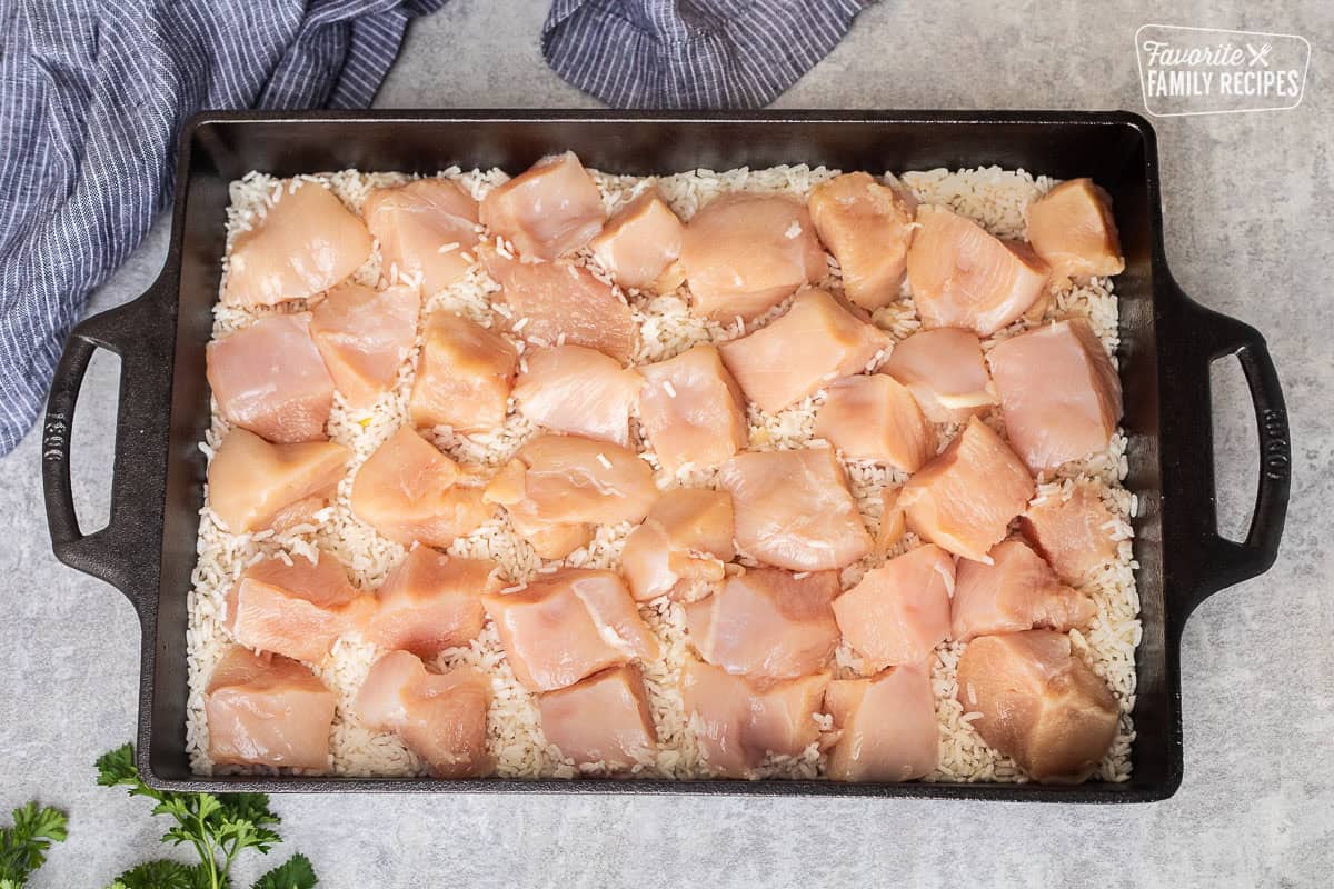 Baking dish with soup mixture topped with rice and large pieces of chicken breast.