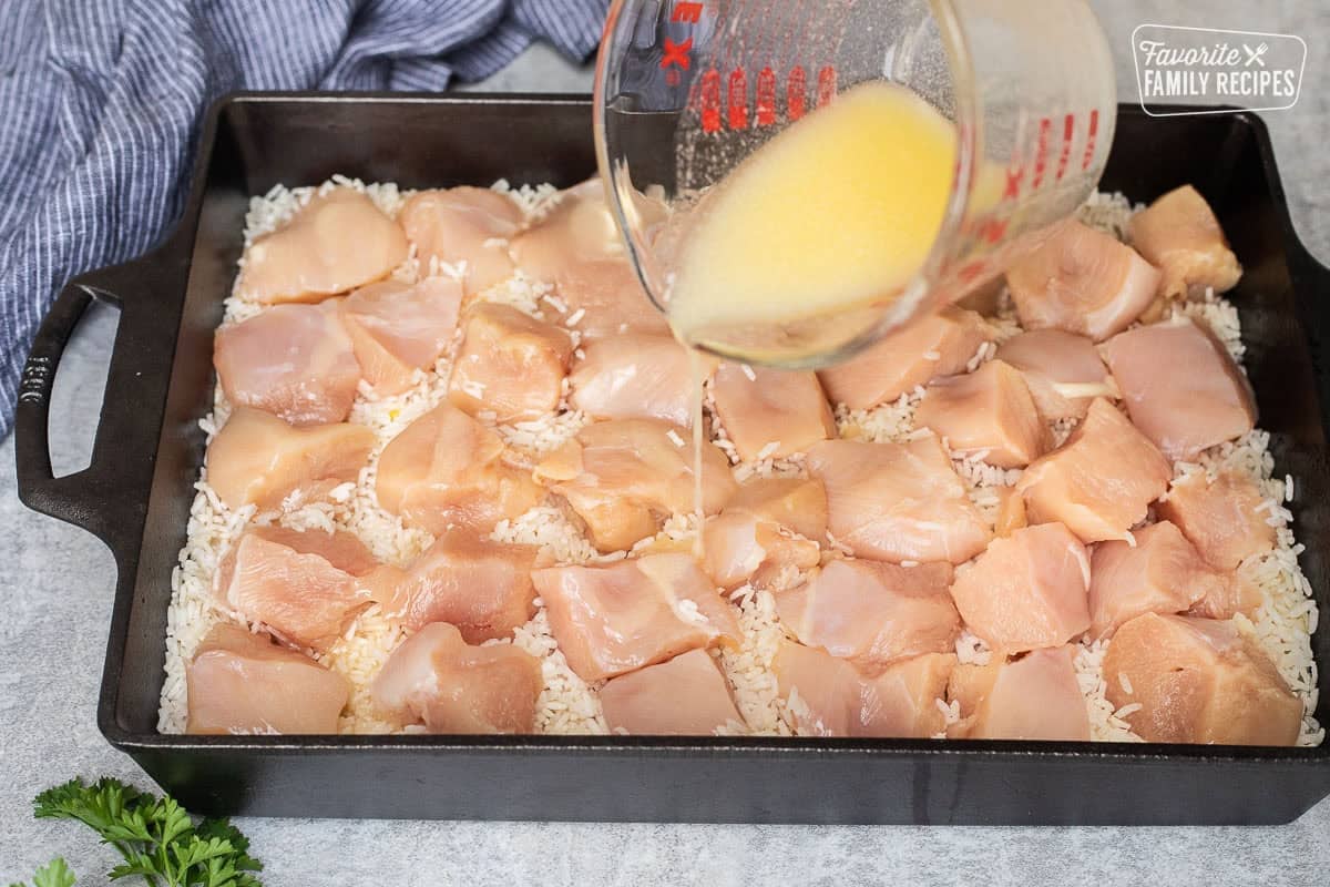 Pouring butter on top of chicken breast pieces in a baking dish over rice and soup mix.