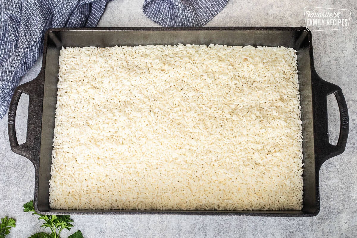 Baking dish with mini white rice over soup mixture.