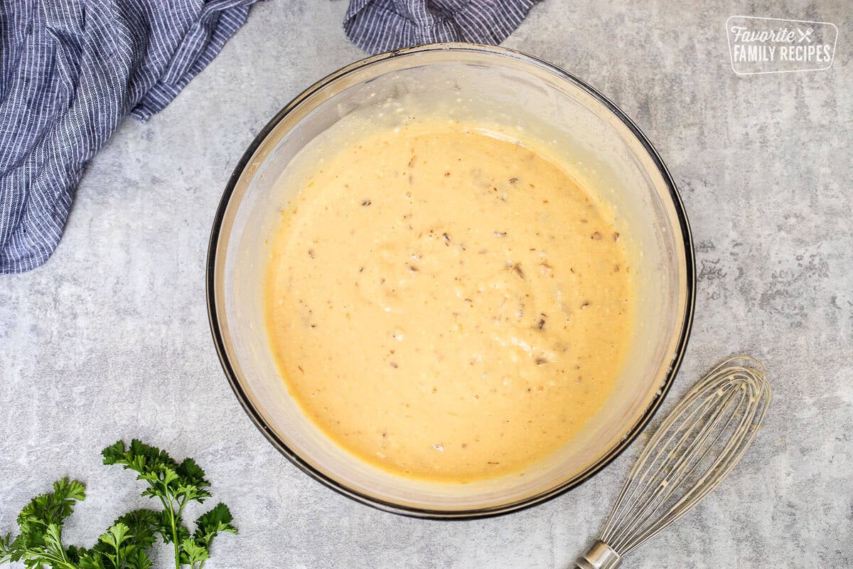 Glass mixing bowl of soup mixture with a whisk on the side.
