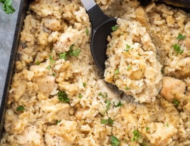 Spoon resting in baking dish of easy chicken casserole.