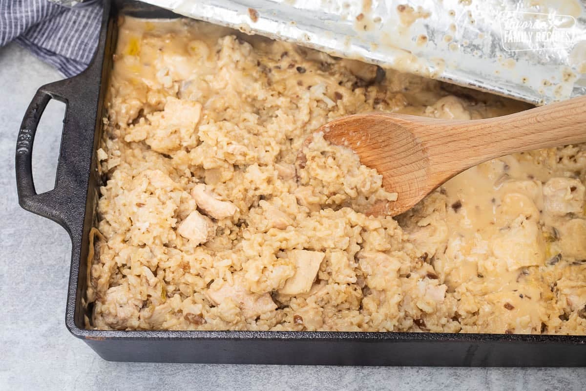 Stirring easy chicken casserole in a baking dish with a wooden spoon.