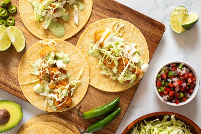 Three Halibut tacos on a wooden board topped with cabbage and cilantro sauce.