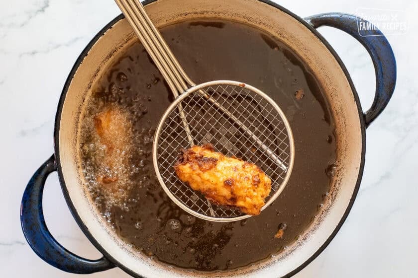 Fried Halibut on a wire strainer over hot oil.
