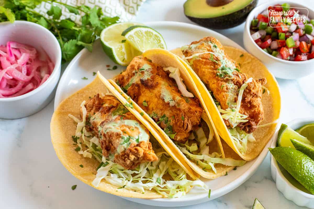 Three halibut tacos on corn tortillas topped with cilantro, cabbage and green sauce.