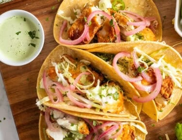 Four halibut tacos on corn tortillas topped with cilantro, cabbage, onion and green sauce.