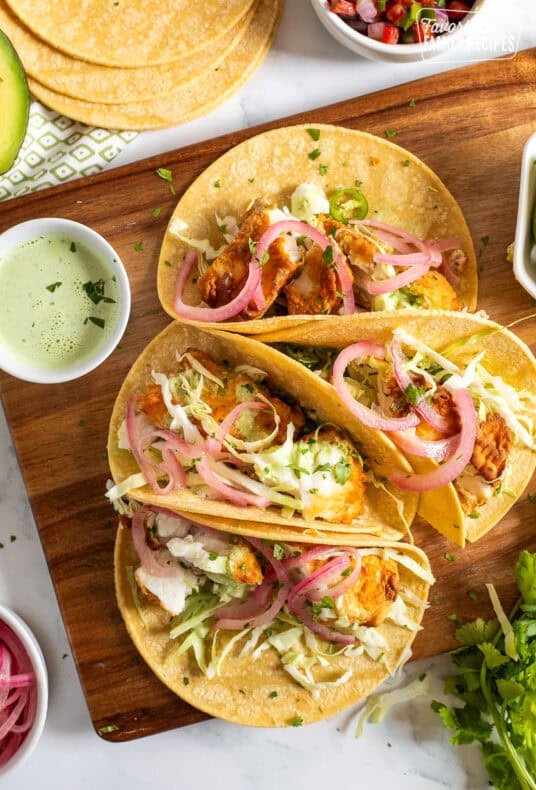 Four halibut tacos on corn tortillas topped with cilantro, cabbage, onion and green sauce.