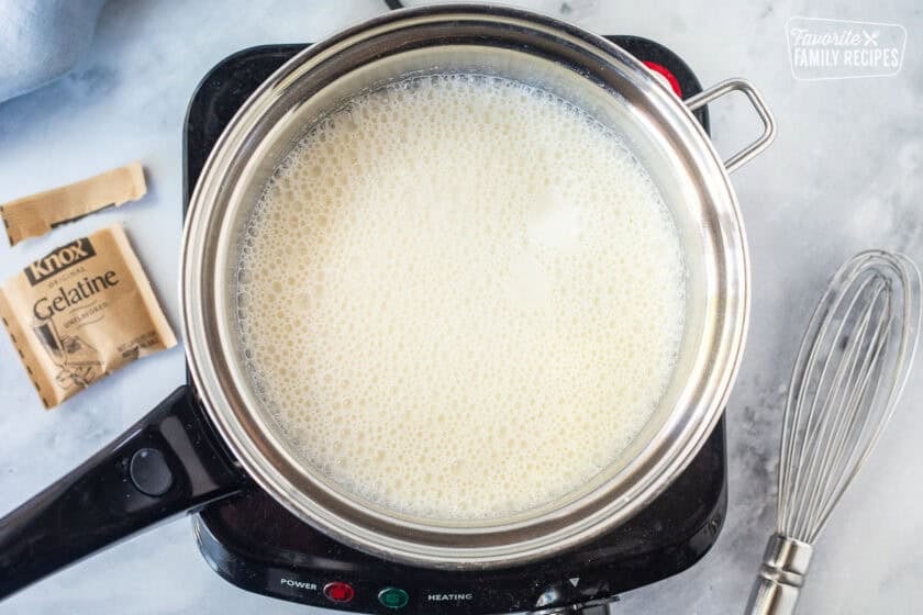 Electric burner with saucepan and cold milk with gelatin. Whisk on the side.