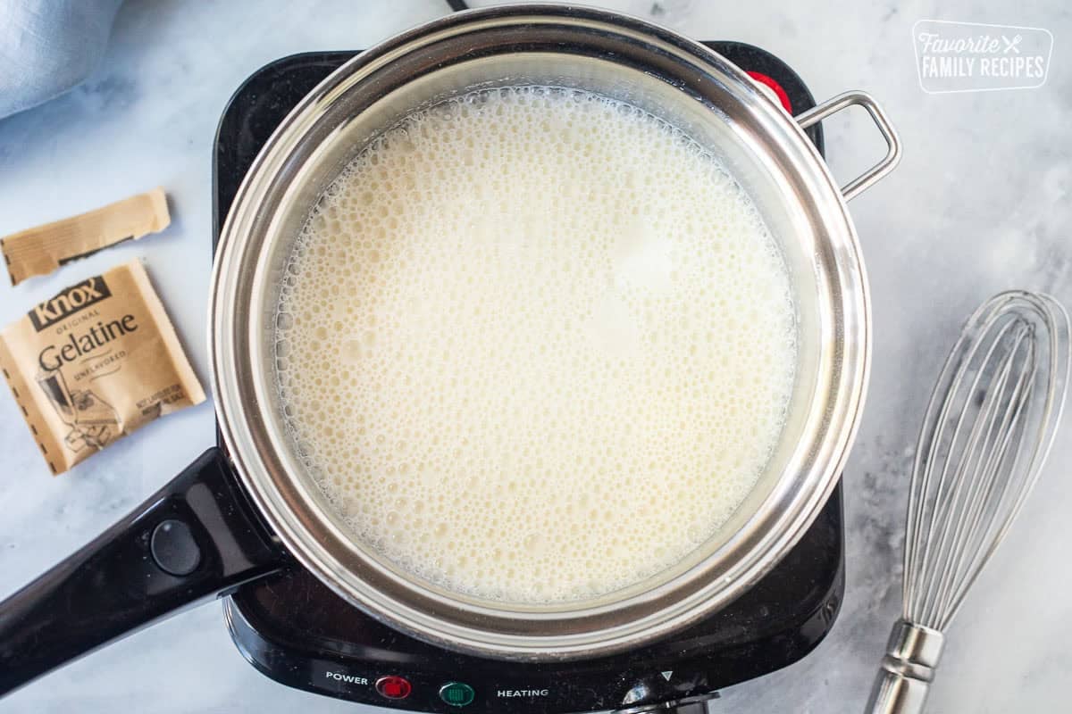 Electric burner with saucepan and cold milk with gelatin. Whisk on the side.