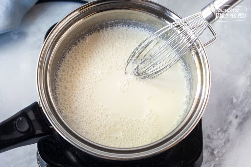 Whisking milk and gelatin in a saucepan on an electric burner.