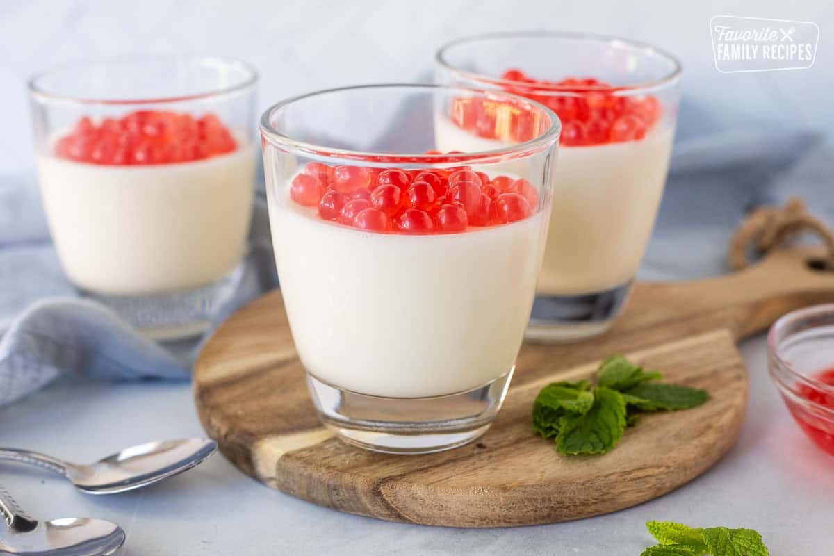 Three glasses of panna cotta topped with strawberry bursting bubbles.