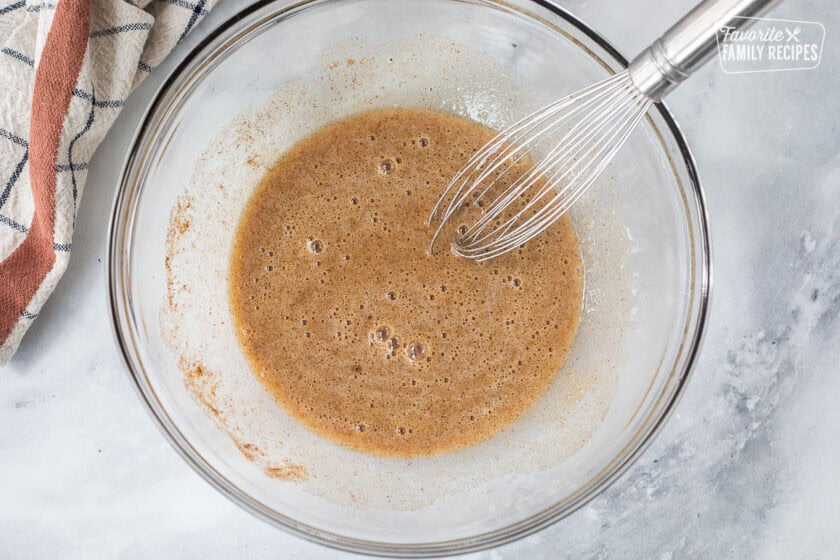 Glass mixing bowl with mixture of eggs and spices to prepare pumpkin pie.