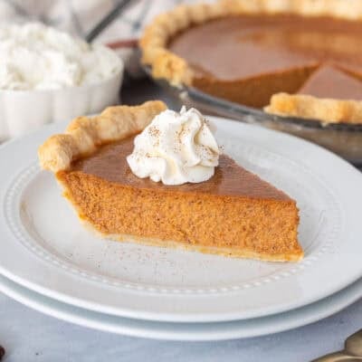 Slice of pumpkin pie on a plate topped with whipped cream and cinnamon.