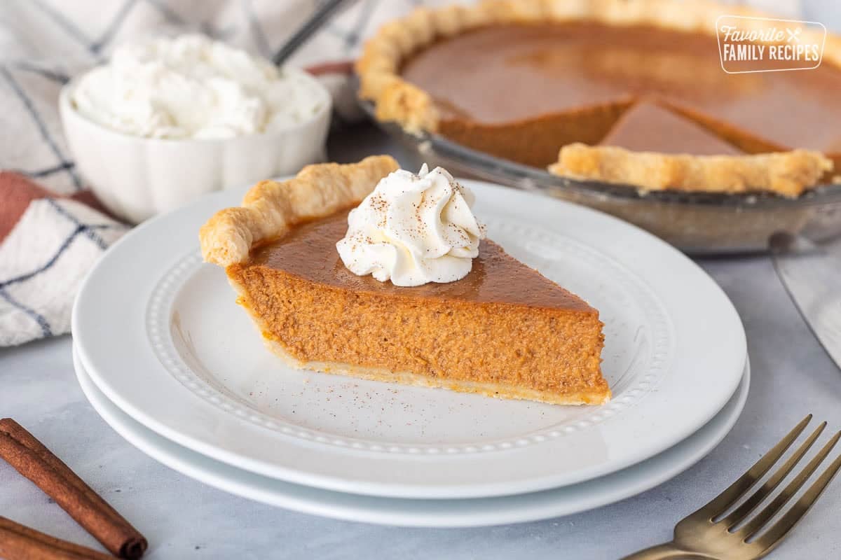 Slice of pumpkin pie on a plate topped with whipped cream and cinnamon.
