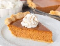 Slice of pumpkin pie on a plate topped with whipped cream and cinnamon.