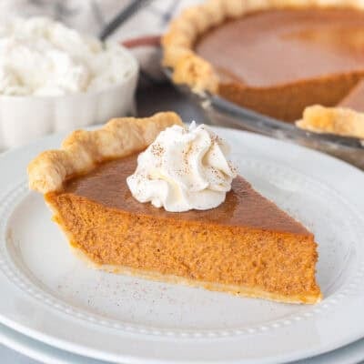 Slice of pumpkin pie on a plate topped with whipped cream and cinnamon.