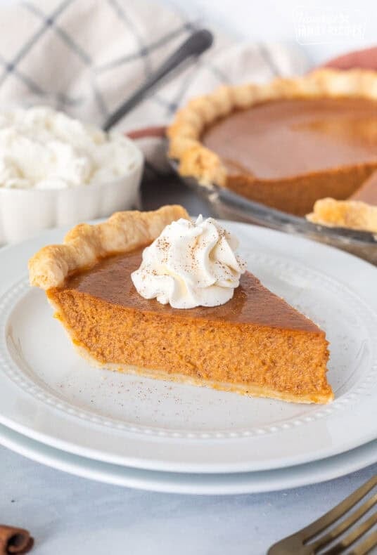 Slice of pumpkin pie on a plate topped with whipped cream and cinnamon.