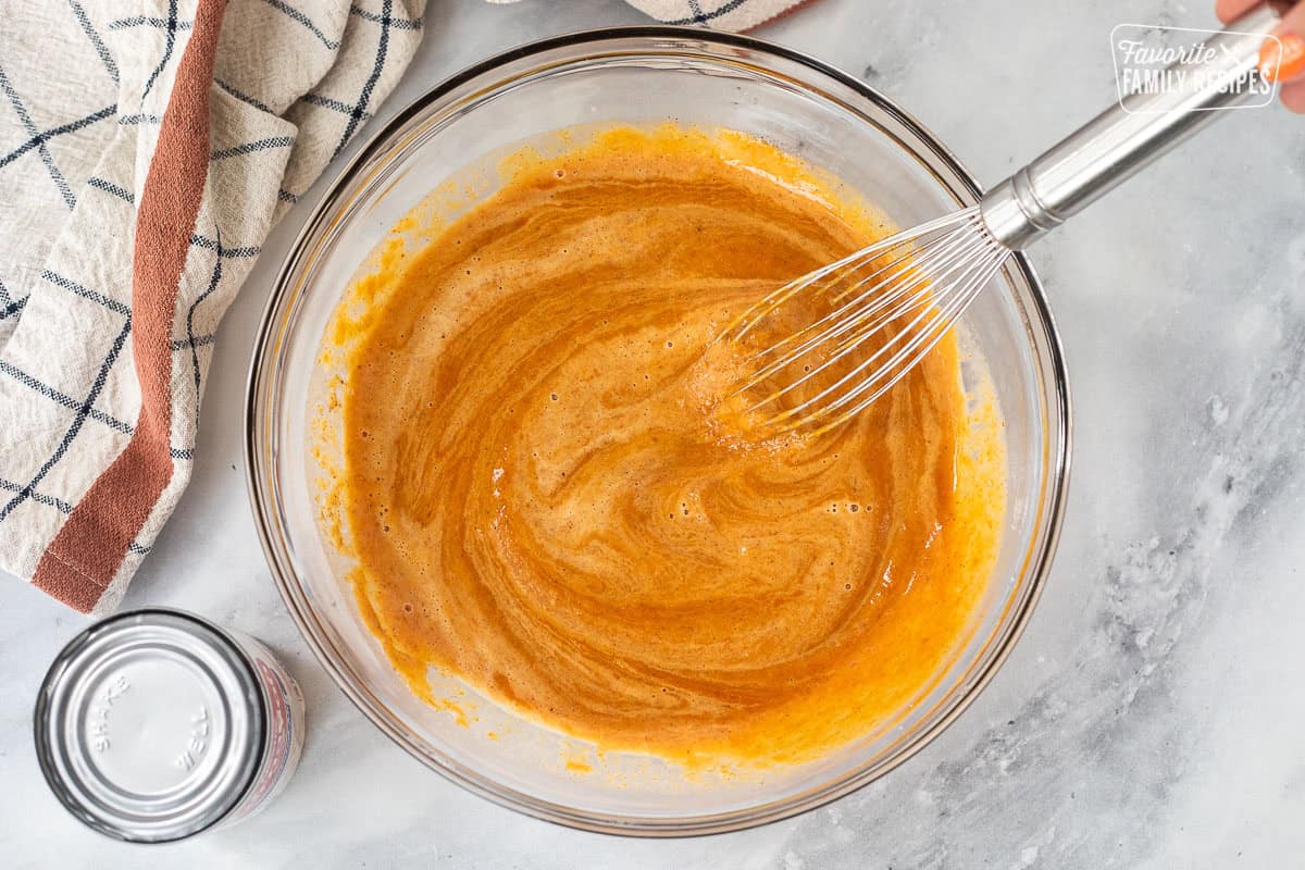 Stirring evaporated milk into a bowl of pumpkin pie filling mixture.