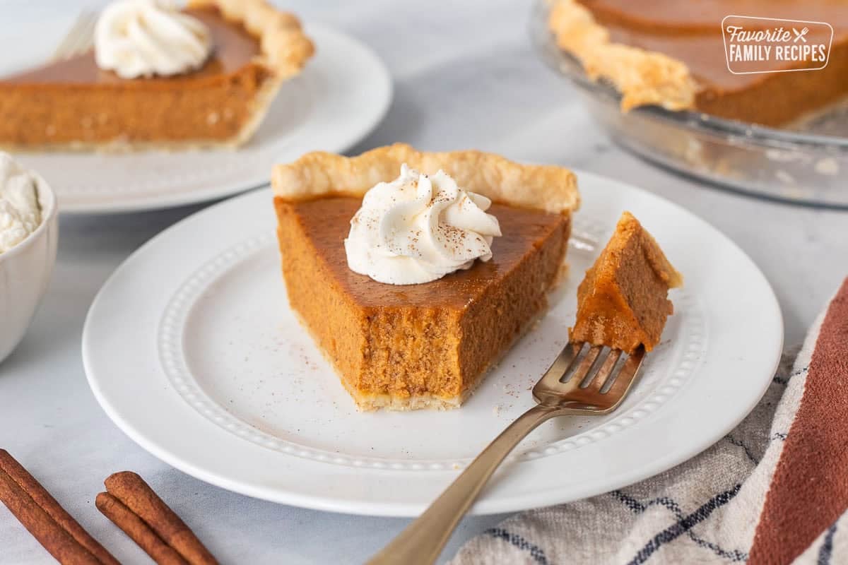 Front point of pumpkin pie slice cut by a fork and resting on a plate.