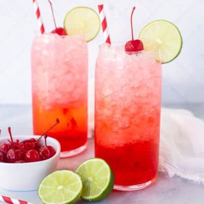 Two glasses of Shirley Temple Drinks garnished with lime slices and cherries.
