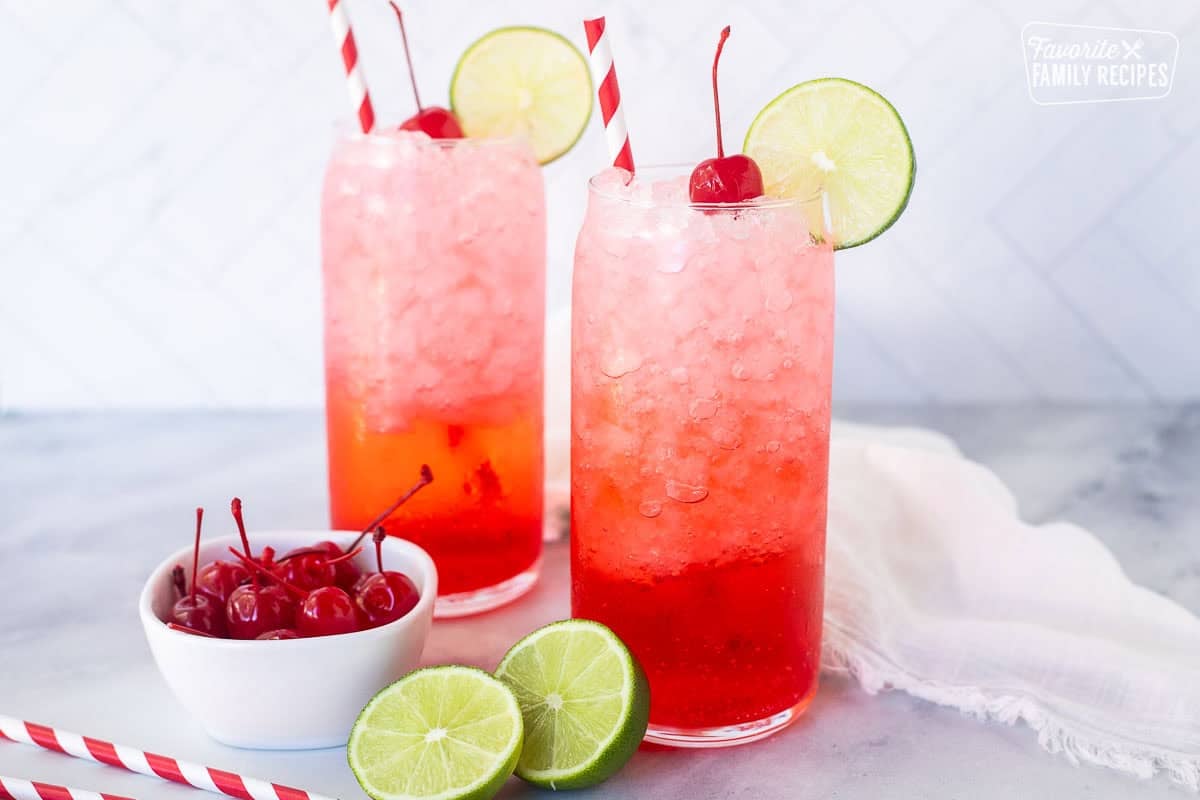 Two glasses of Shirley Temple Drinks garnished with lime slices and cherries.